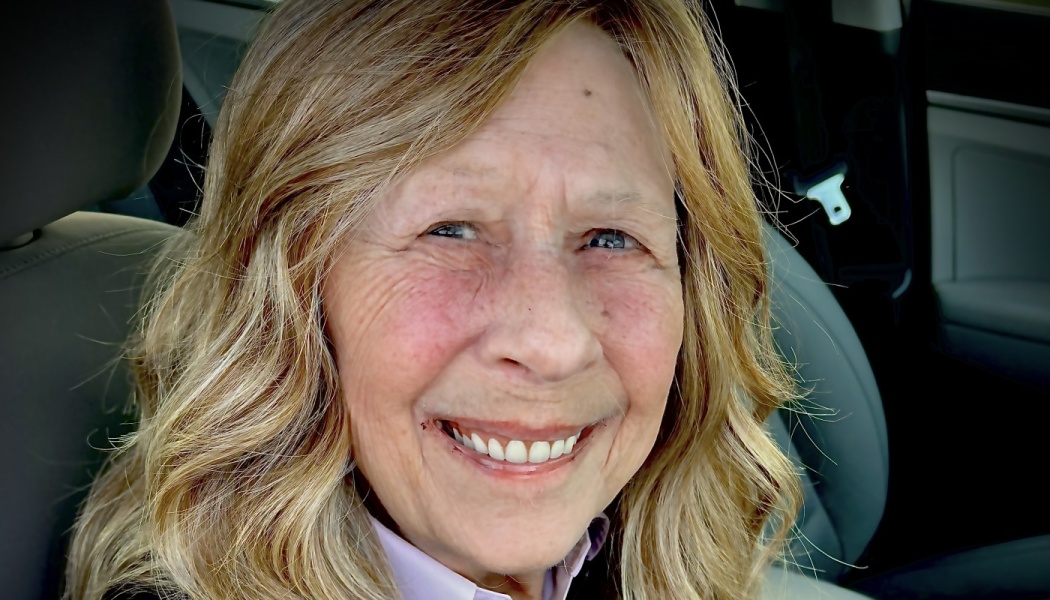 Close-up portrait of a smiling senior woman with wavy blonde hair inside a car.