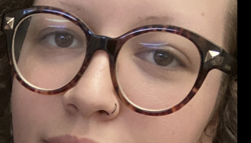 Close-up of a person wearing round tortoiseshell glasses and a small black nose ring.