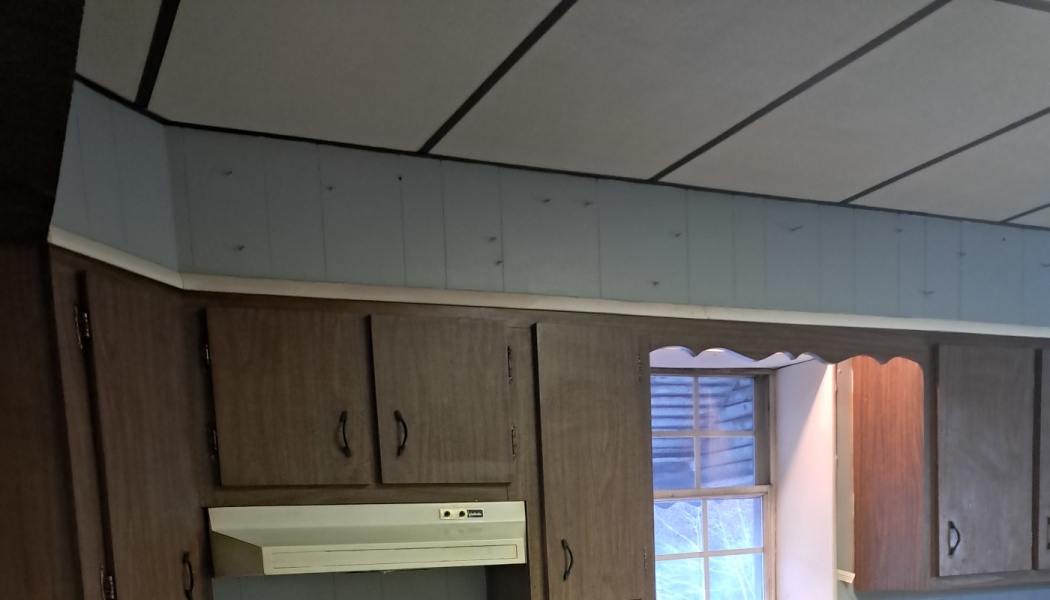 Outdated dark wood kitchen cabinets with a white range hood beneath a drop ceiling and blue soffit.