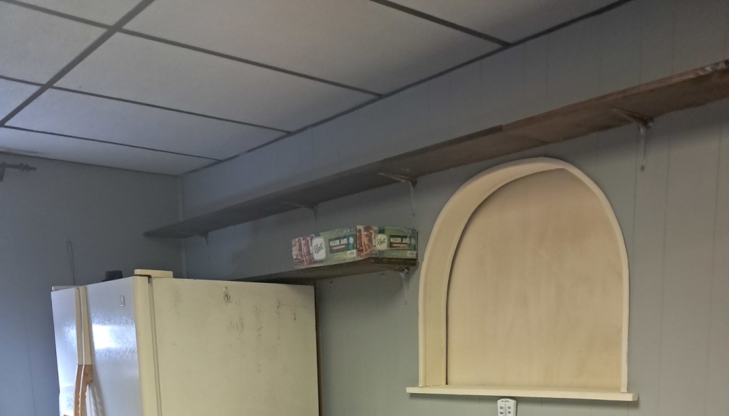 An arched wall niche next to a white refrigerator, with high wooden shelves holding boxes of mason jars.