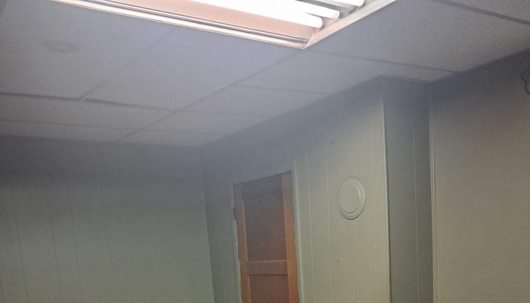 Dimly lit room with paneled walls, a wooden door, and bright overhead fluorescent light.