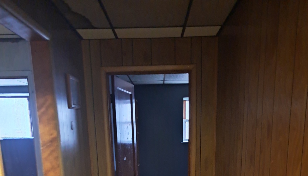 Wood-paneled hallway with severe smoke and water damage on ceiling tiles leading into a dark, fire-damaged room.