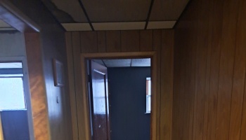Wood-paneled hallway with severe smoke and water damage on ceiling tiles leading into a dark, fire-damaged room.