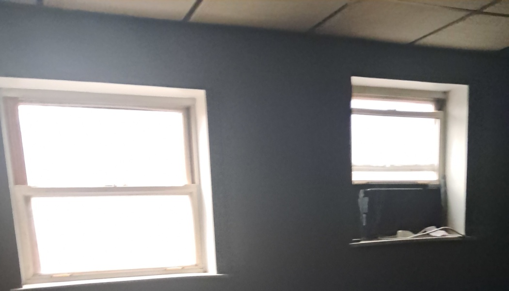 Interior dark grey wall with two bright double-hung windows, one with a small window AC unit.
