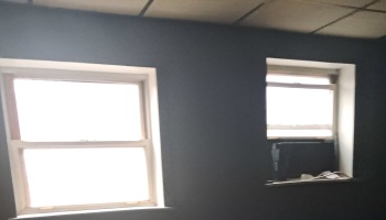 Interior dark grey wall with two bright double-hung windows, one with a small window AC unit.