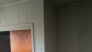 Dim interior corner showing white wall paneling, a wooden door trim, and shadowed walls.