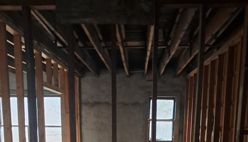 Exposed wooden wall studs and ceiling joists inside an unfinished, gutted room under renovation.
