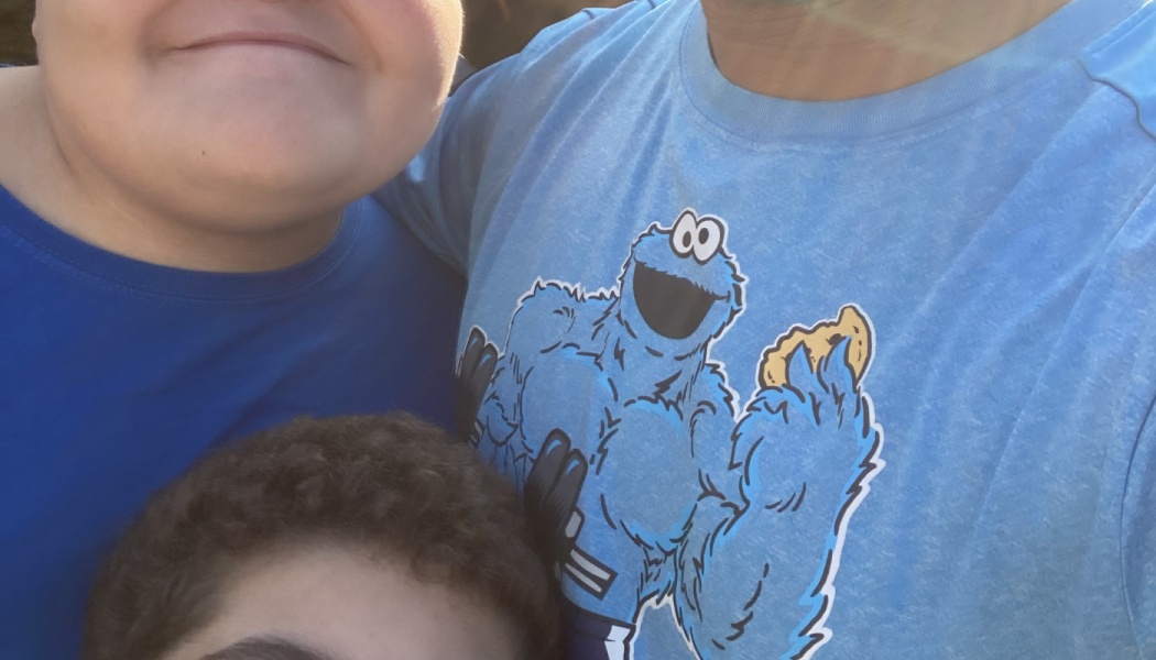Close-up selfie of family members, featuring a light blue t-shirt with a muscular Cookie Monster graphic.