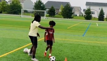 A coach guides a young boy during a soccer training session on a turf field.