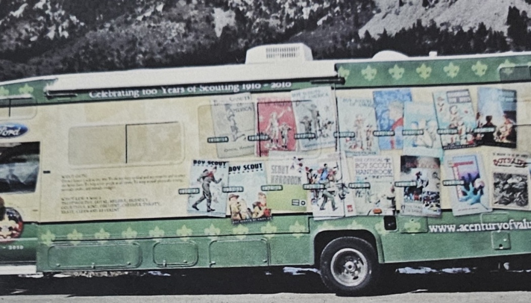 A green RV decorated with vintage Boy Scout handbook covers, celebrating 100 years of Scouting.