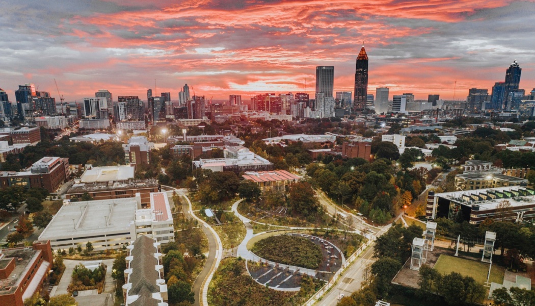 Aerial view of the Atlanta skyline and campus parks under a vibrant, fiery orange sunset sky.
