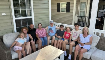 A large, multi-generational family smiling together while sitting on an outdoor patio sectional sofa.
