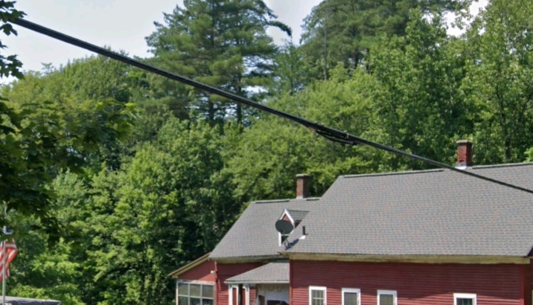 Red building with a grey roof surrounded by dense green forest, with utility lines extending across the foreground.