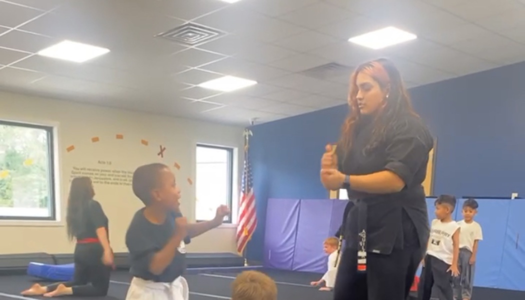 A martial arts instructor with a black belt demonstrates techniques to a young boy in a studio class.