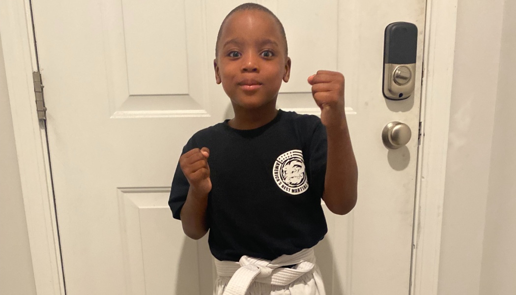 Young boy in a martial arts uniform with a white belt posing proudly with raised fists.