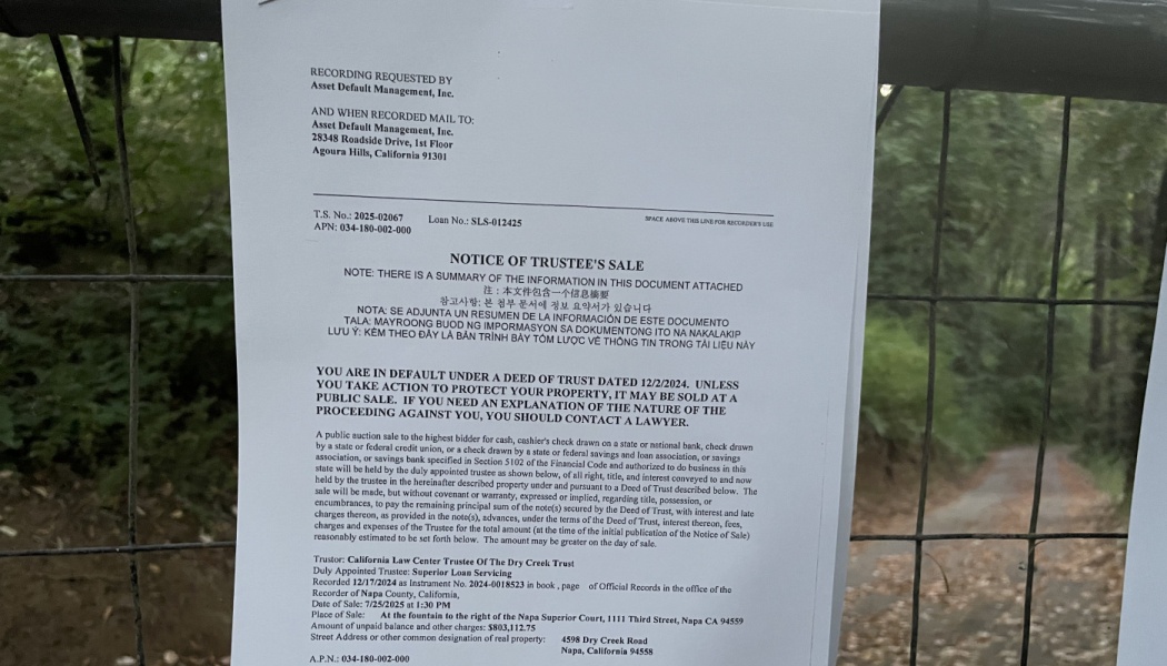 Notice of Trustee's Sale legal document posted on a wire fence in front of a wooded property.