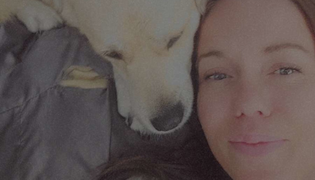 Close-up of a woman smiling gently while lying next to her sleeping yellow dog.