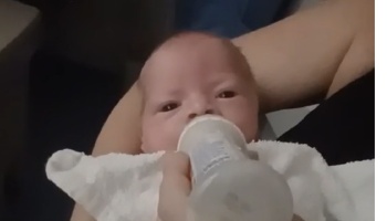 A newborn baby drinking milk from a bottle held by an adult.