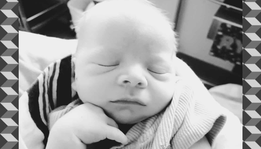 Black and white close-up of a newborn baby sleeping peacefully with a tiny hand resting under its chin.