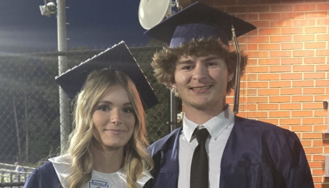 Two young graduates smiling together in navy blue caps and gowns at night.