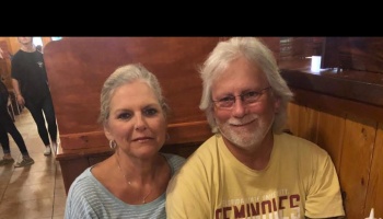 A smiling older couple sitting together in a wooden restaurant booth, the man wearing glasses and a beard.