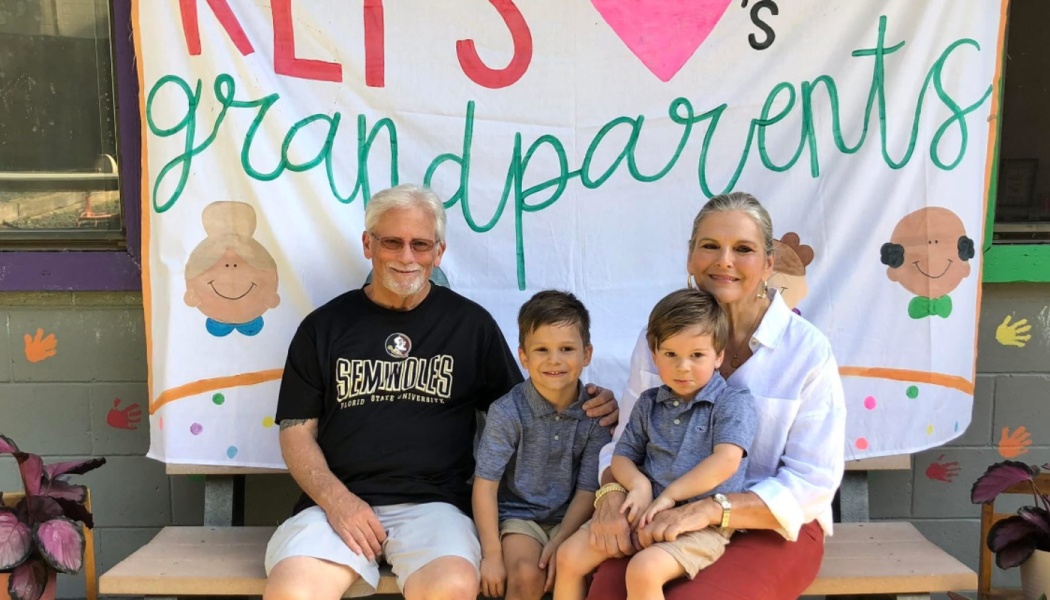 Grandparents sitting on a bench with two young grandsons in front of a handmade banner.
