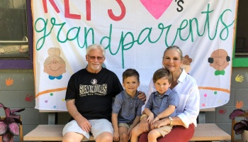 Grandparents sitting on a bench with two young grandsons in front of a handmade banner.