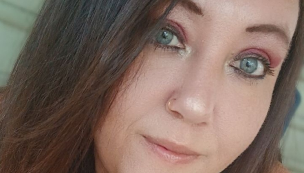 Close-up portrait of a woman with dark hair, bright blue eyes, eyeshadow, and a nose ring.