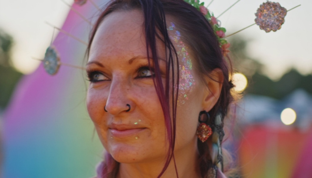 Close-up of a smiling woman wearing face glitter, a septum ring, and a decorative sunburst headpiece.
