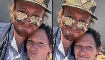 A bearded man in aviator sunglasses and a cap poses affectionately close to a dark-haired woman.