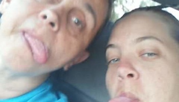 Close-up selfie of two people playfully sticking their tongues out at the camera.