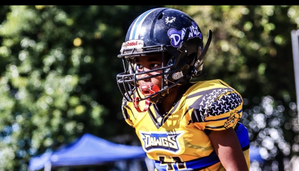 Young football player wearing a black helmet, red mouthguard, and yellow Dawgz uniform looking focused.