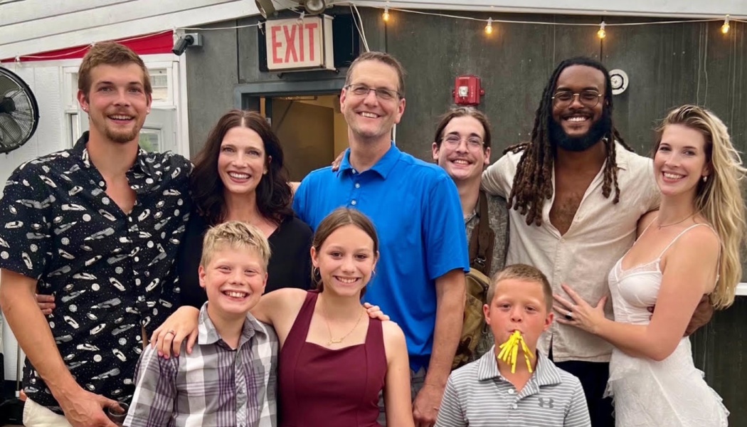 A smiling group of eight diverse adults and children posing together outdoors.