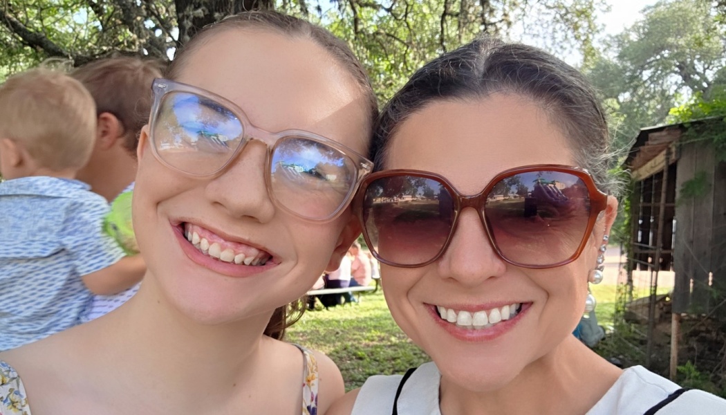 A young girl with glasses and a woman wearing sunglasses smile closely for an outdoor selfie.