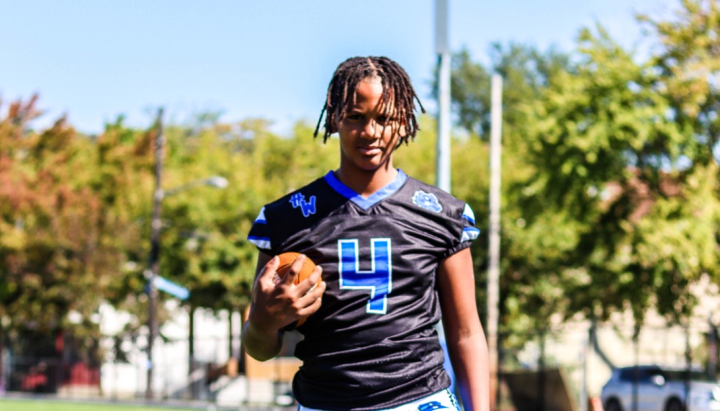 Young football player with locs wearing a black and blue number 4 jersey while holding a football.