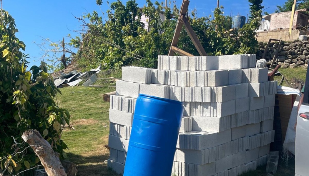 A stack of concrete cinder blocks and a blue plastic barrel outdoors on a grassy hill, ready for rebuilding.