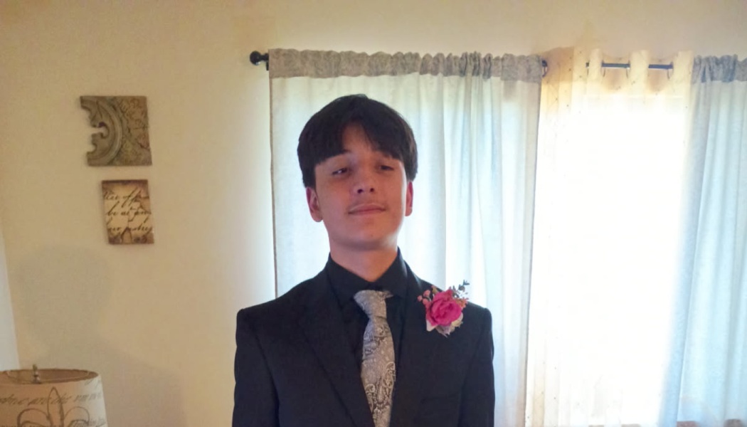 Young man dressed in a black suit with a patterned grey tie and pink rose boutonniere on his lapel.