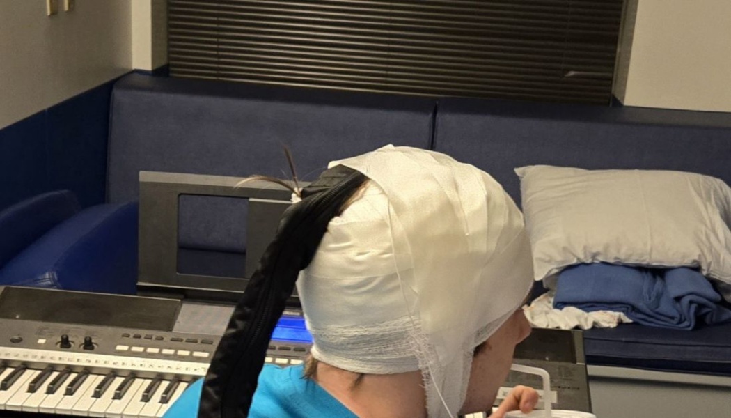 A person with a bandaged head sitting in front of an electronic keyboard in a hospital room.