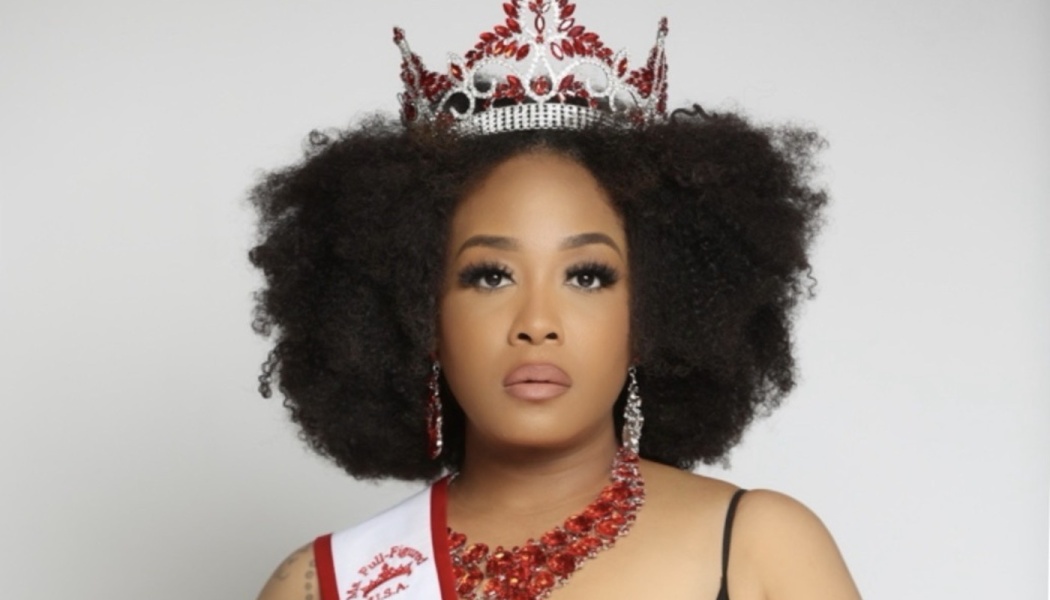 A Black woman with an afro wearing a red and silver crown, red jewel necklace, and pageantry sash.