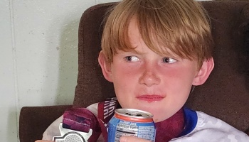 Young blonde boy with flushed cheeks holding a juice can and wearing a medal around his neck.