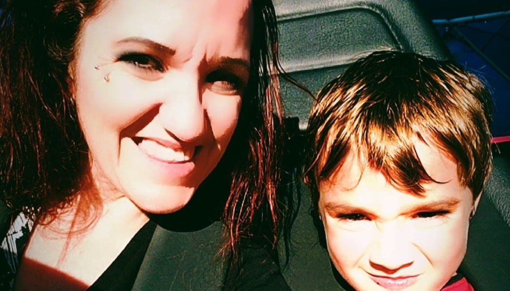 A smiling dark-haired woman and a young boy squinting playfully in the bright sun.