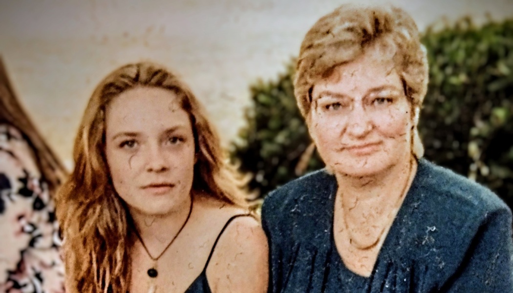A young woman with long wavy hair sitting beside an older woman in a blue jacket.