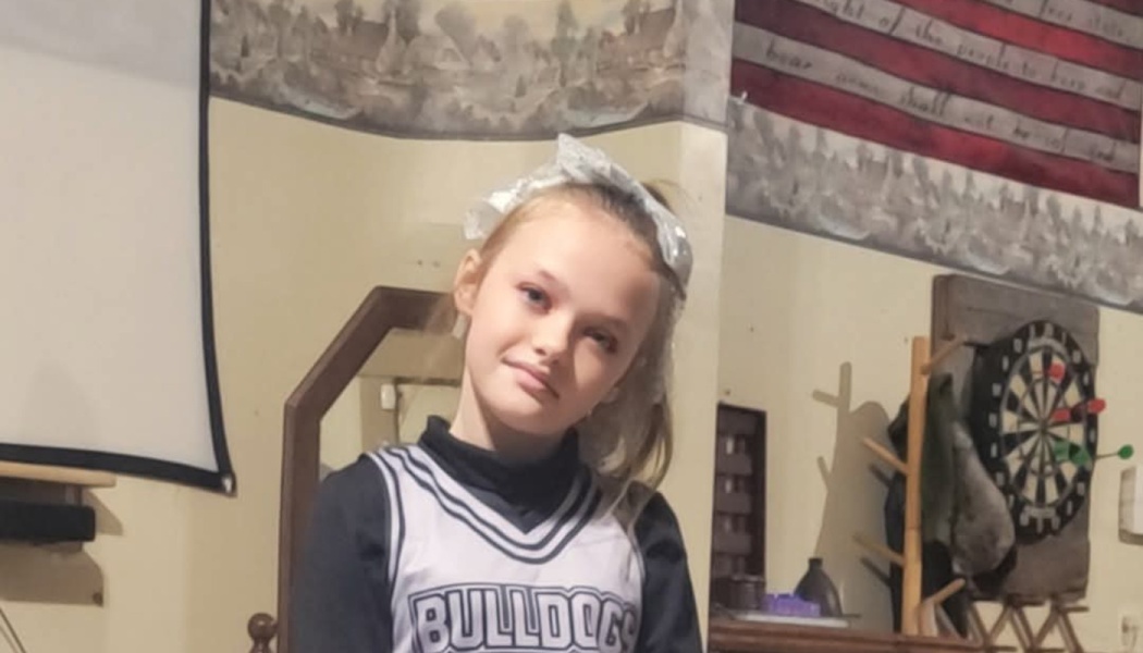 Young girl smiling softly in a black and white Bulldogs cheerleader uniform with a white hair bow.