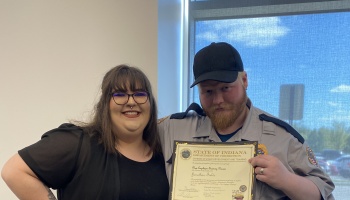 A smiling woman stands beside a man in uniform holding an Indiana Department of Correction certificate.
