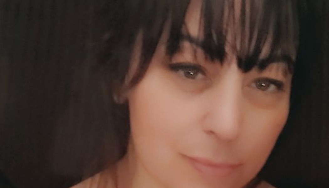 Close-up portrait of a woman with dark hair and bangs looking at the camera with a gentle smile.