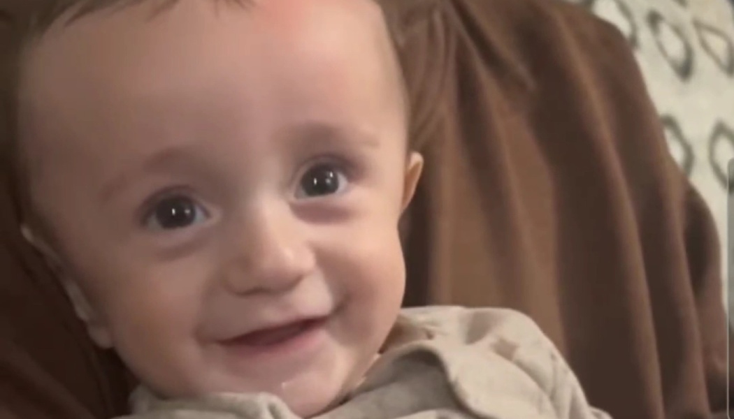 Close-up of a smiling baby with large, dark eyes looking happily at the camera.