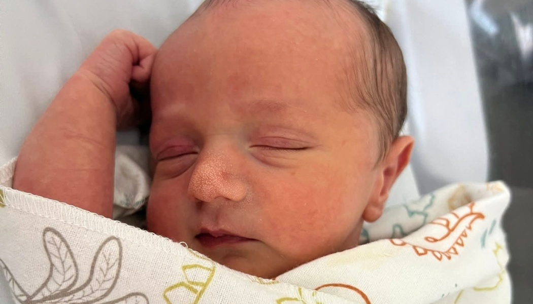 Sleeping newborn baby swaddled in a patterned blanket with a tiny fist raised by their head.