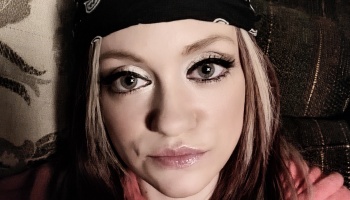 Close-up selfie of a woman with blonde highlights wearing a black bandana headband and eye makeup.