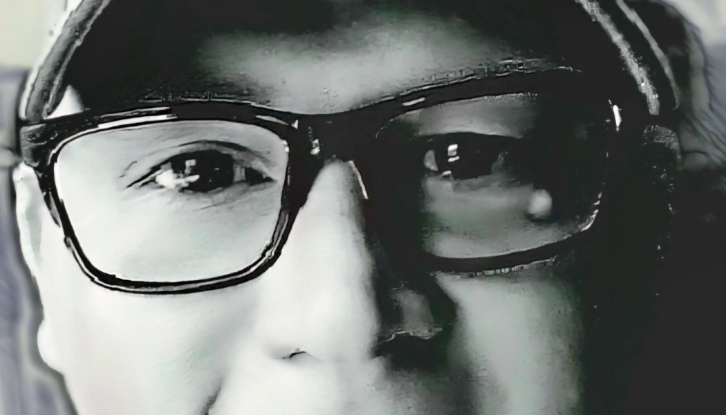 Close-up black-and-white portrait of a person wearing dark-framed glasses and a cap.