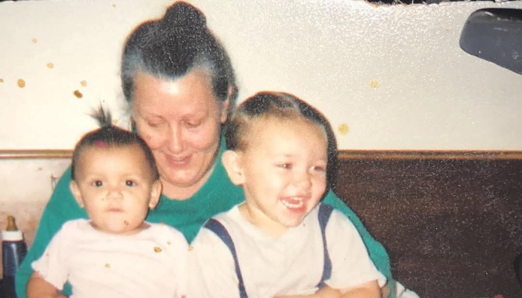 A smiling woman in a green shirt holding a baby and a laughing young boy.